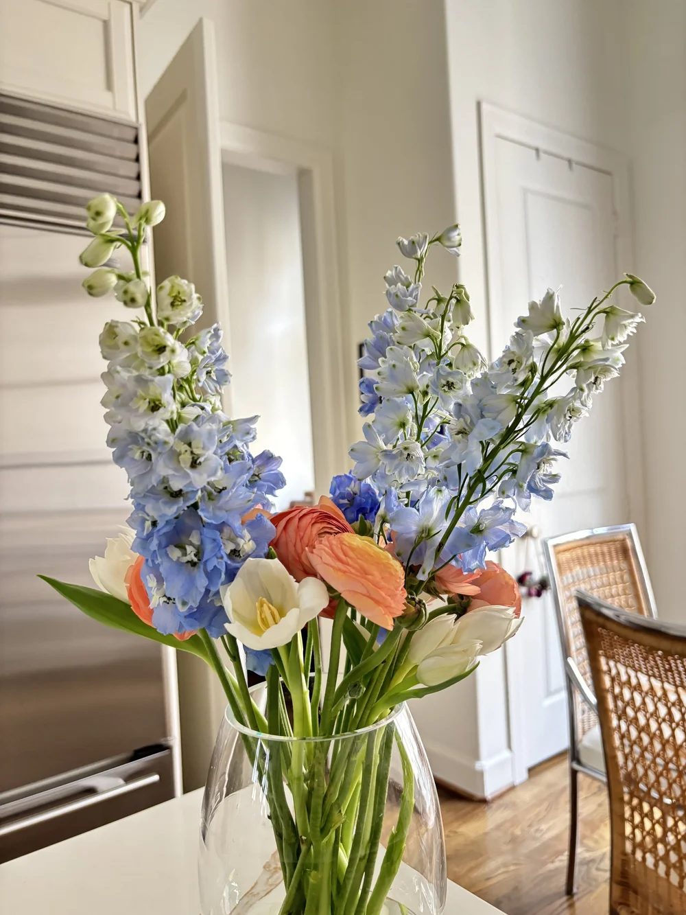 Pale blue delphinium and orange tulips against a white door