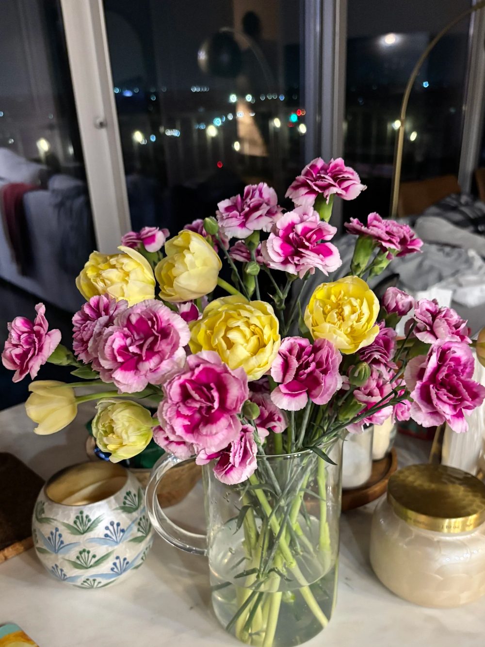 Magenta carnations and yellow tulips beside a night window