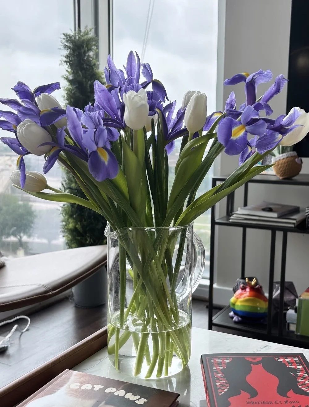 Purple iris and white tulips in a tall glass cylinder